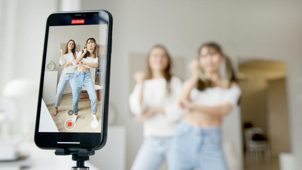 Two women dance in front of a smartphone camera, recording showing the way of content creation of jkdigitalworks